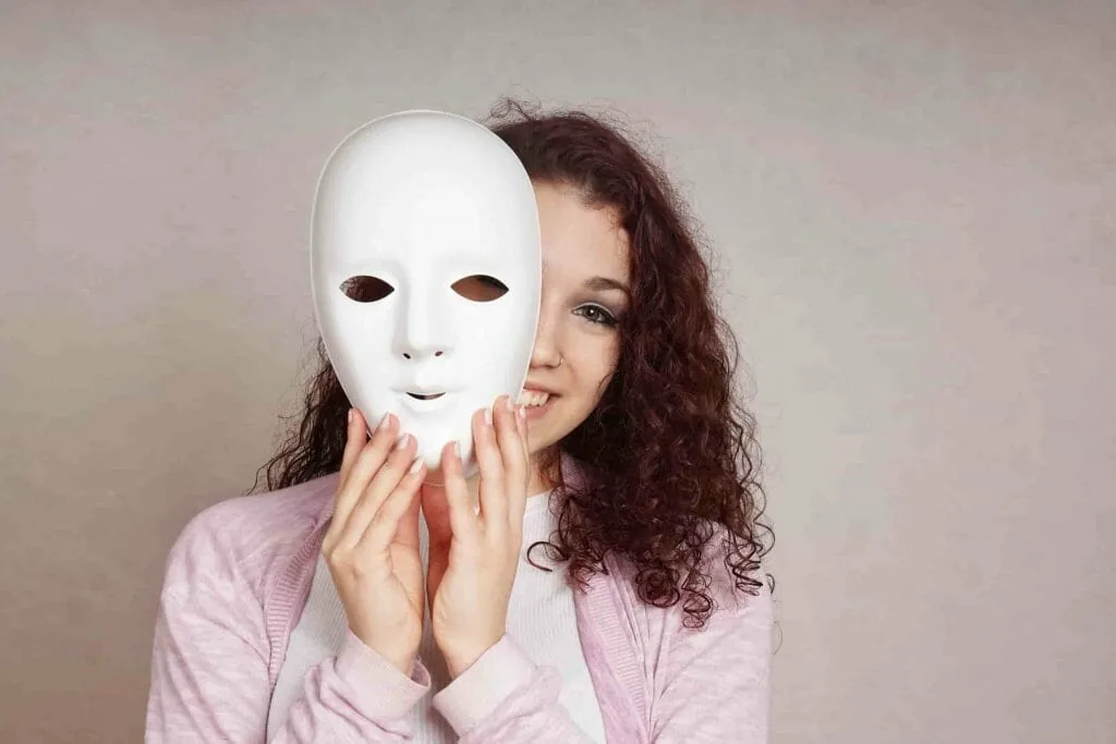 Identity and the masks we wear: a smiling young woman lowering a white mask from her face
