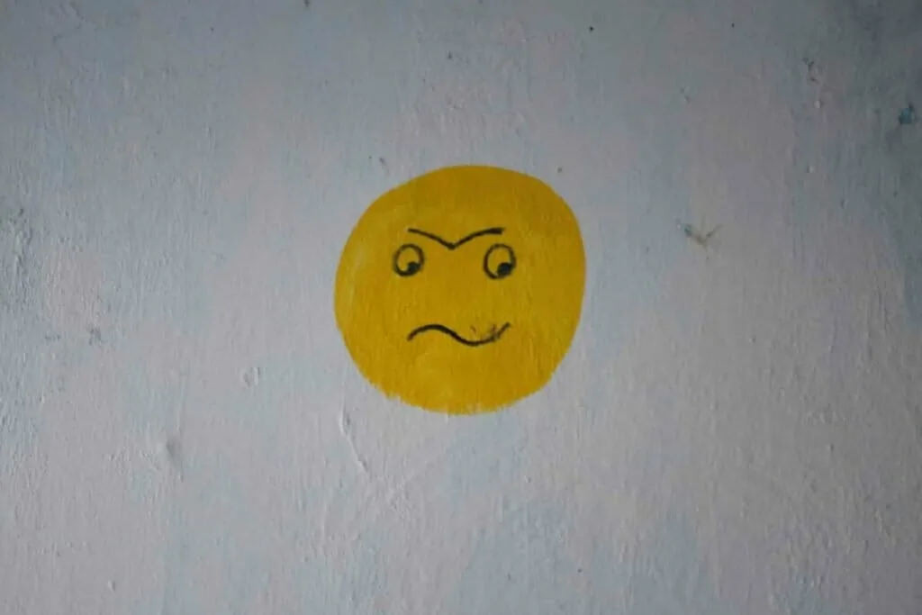 Shadow work prompts for anger and triggers: a grumpy face painted in yellow on a pale wall