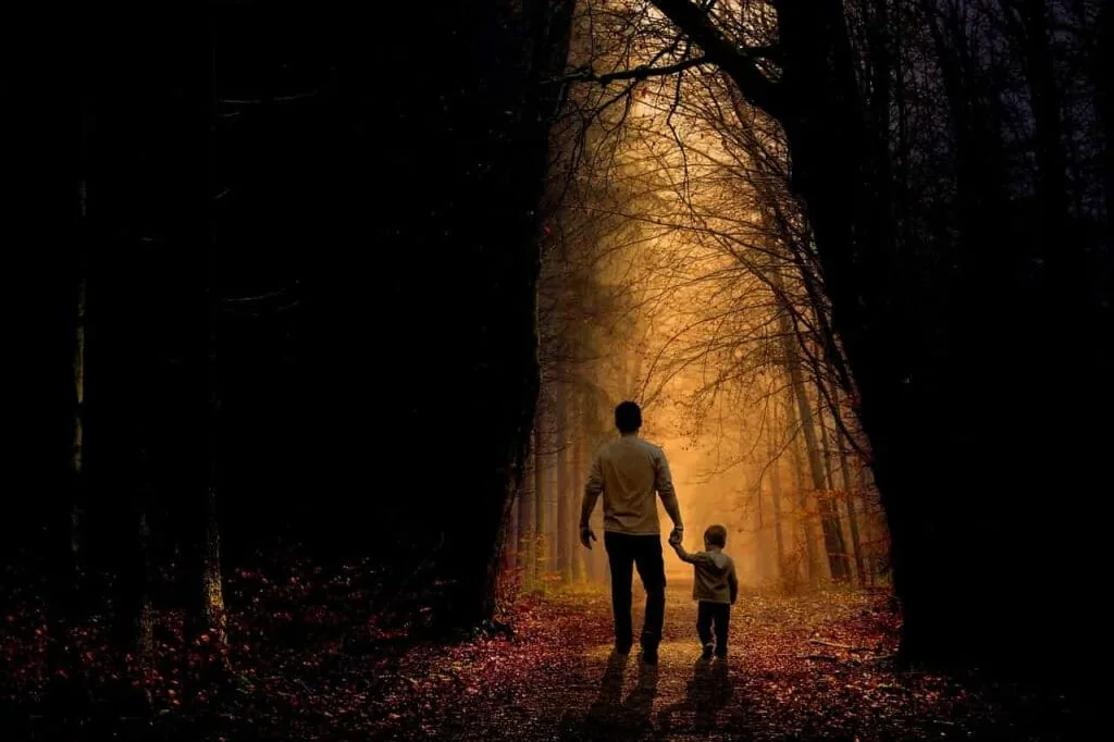 Shadow work questions about childhood: a father and a small child walking hand in hand along a forest path towards the light