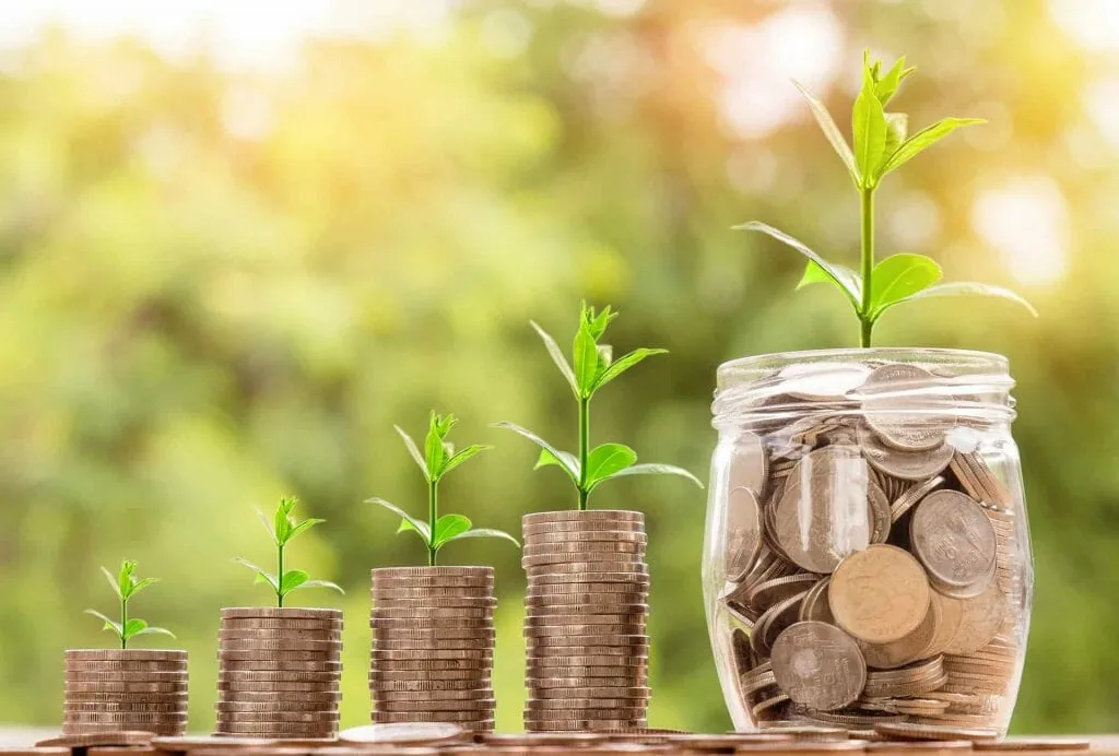 Seek wealth, not quick money: stacks of coins growing taller with green seedlings, beside a glass jar full of coins