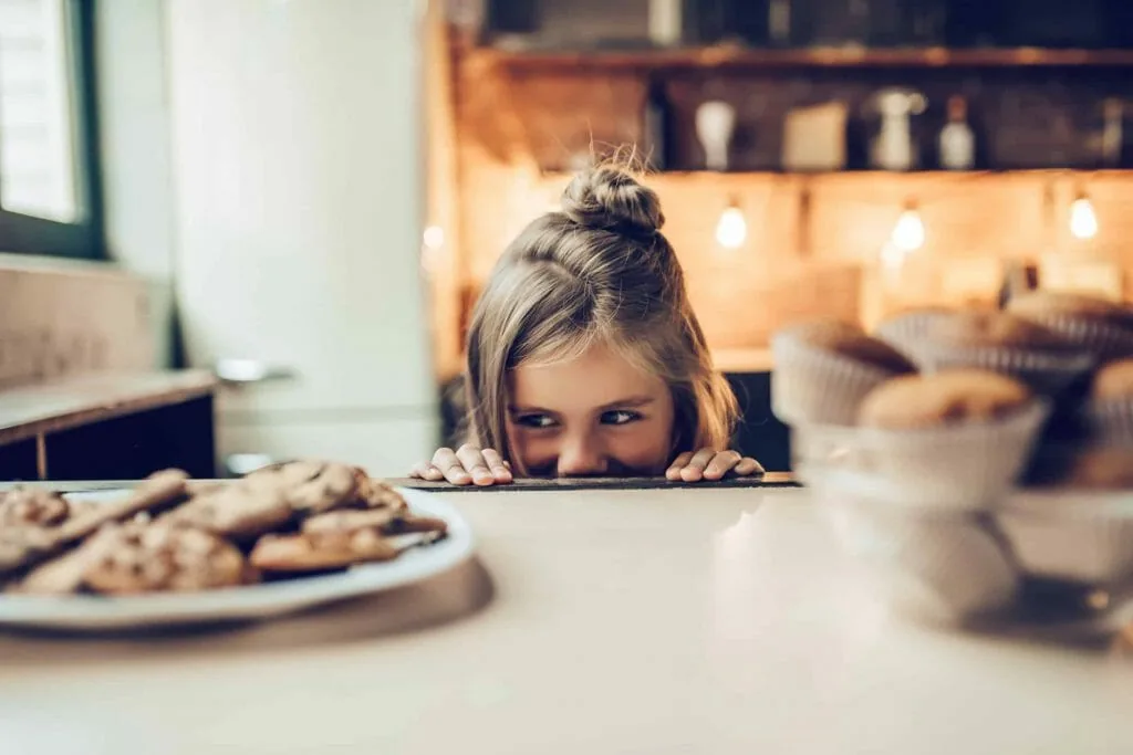 Waiting for the reward: a young girl peeks over a kitchen counter at a plate of cookies