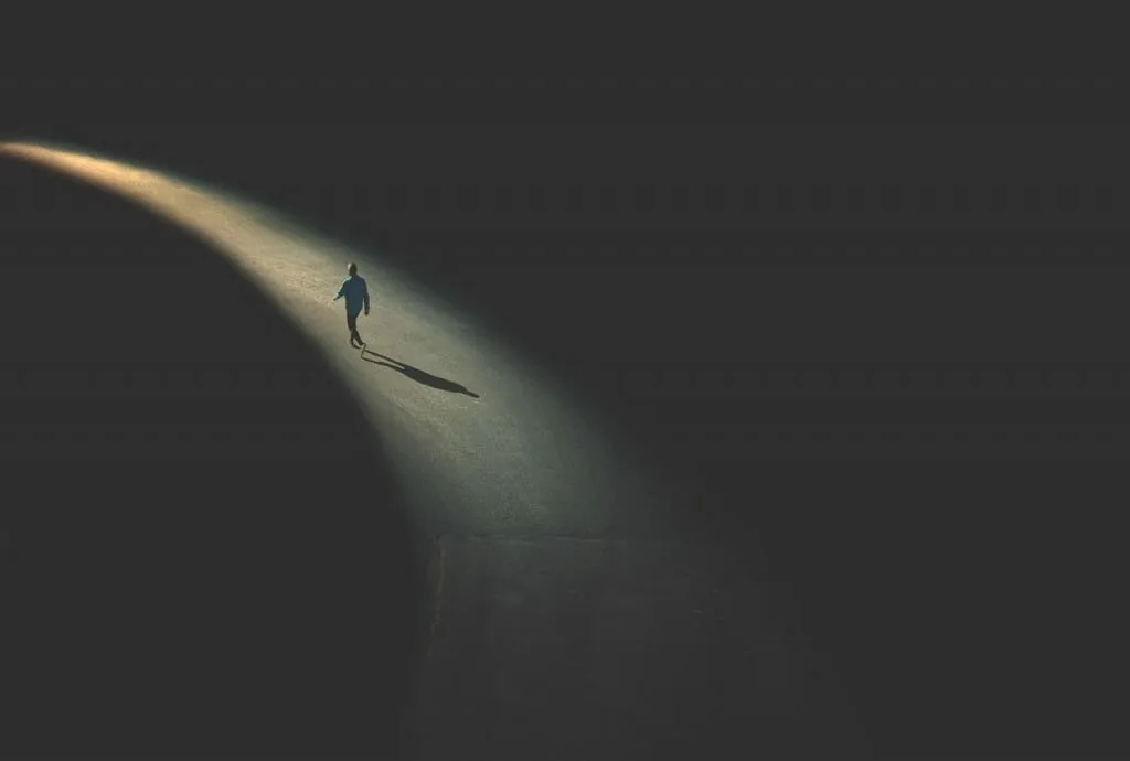 A lone small figure walking along a curved beam of light through the dark, a picture of why the familiar past can feel safer than the unknown future