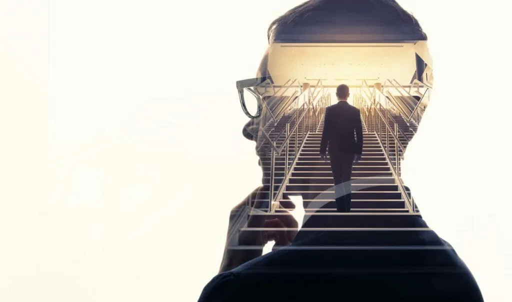 Realist vs visionary meaning: a man's thoughtful profile with a figure inside it climbing a bright staircase towards the light