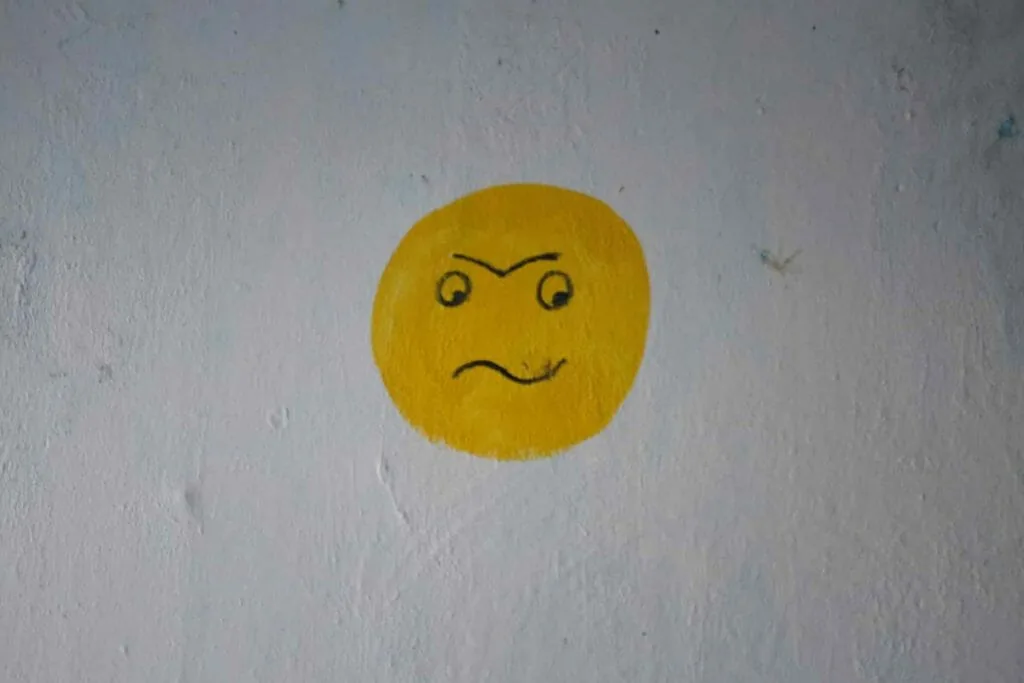 A grumpy yellow face painted on a white wall, like the cold, rigid body language of people ignoring you