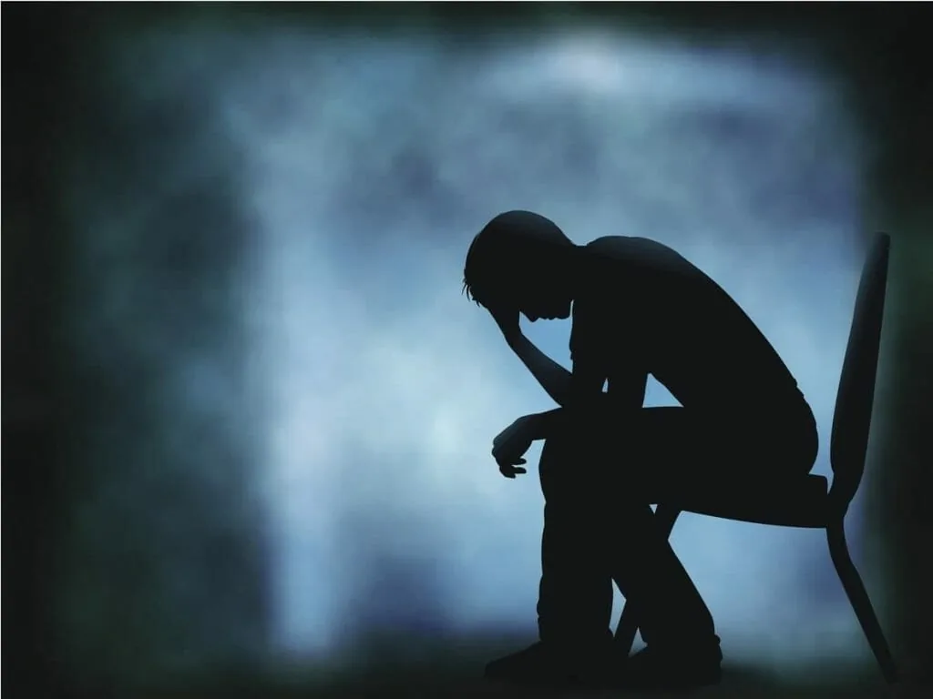 Disrespect and risk taking: the dark silhouette of a person sitting on a chair with head in hand, weighed down by doubt