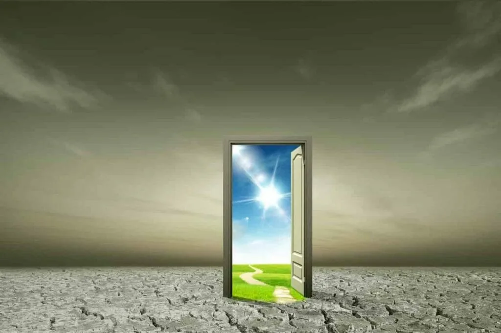How to start over step by step: an open door standing alone in a cracked grey desert, showing green grass and sunshine on the other side