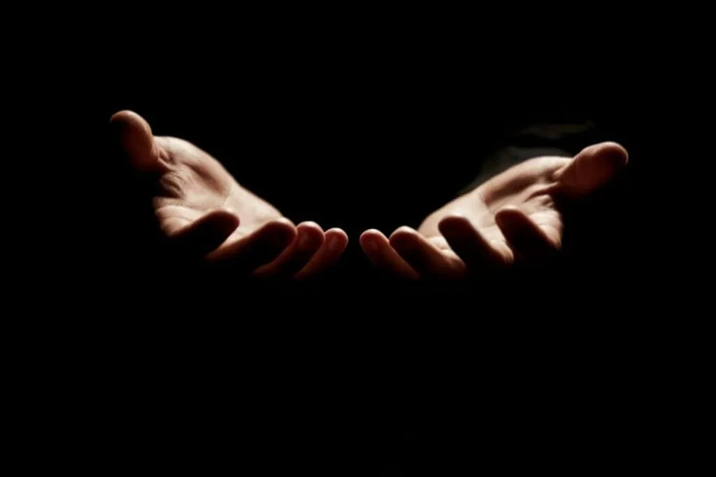 Two open hands held out palms up in the dark, ready to give and receive, like the belief that the energy we give comes back