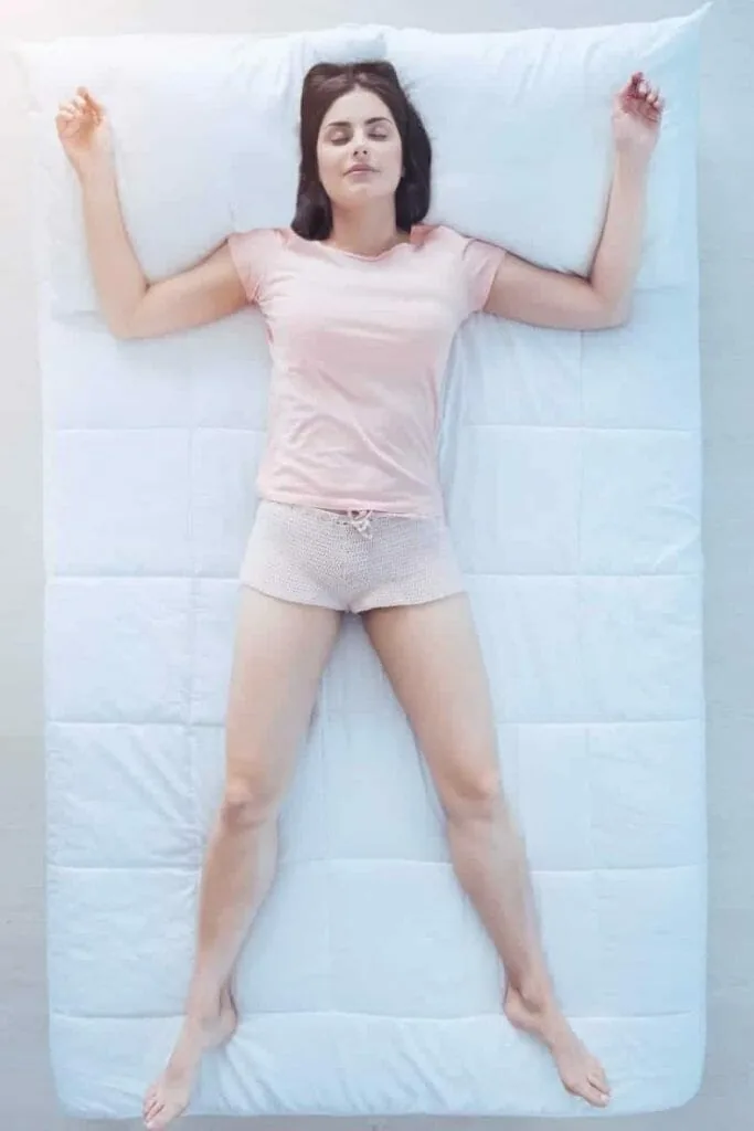Raven method shifting starfish position: a woman lying on her back on a white bed with her arms and legs spread apart, eyes closed