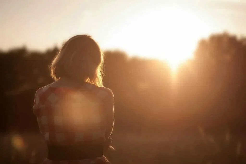 Steadying yourself before starting over: a woman seen from behind, sitting quietly in a field at sunset