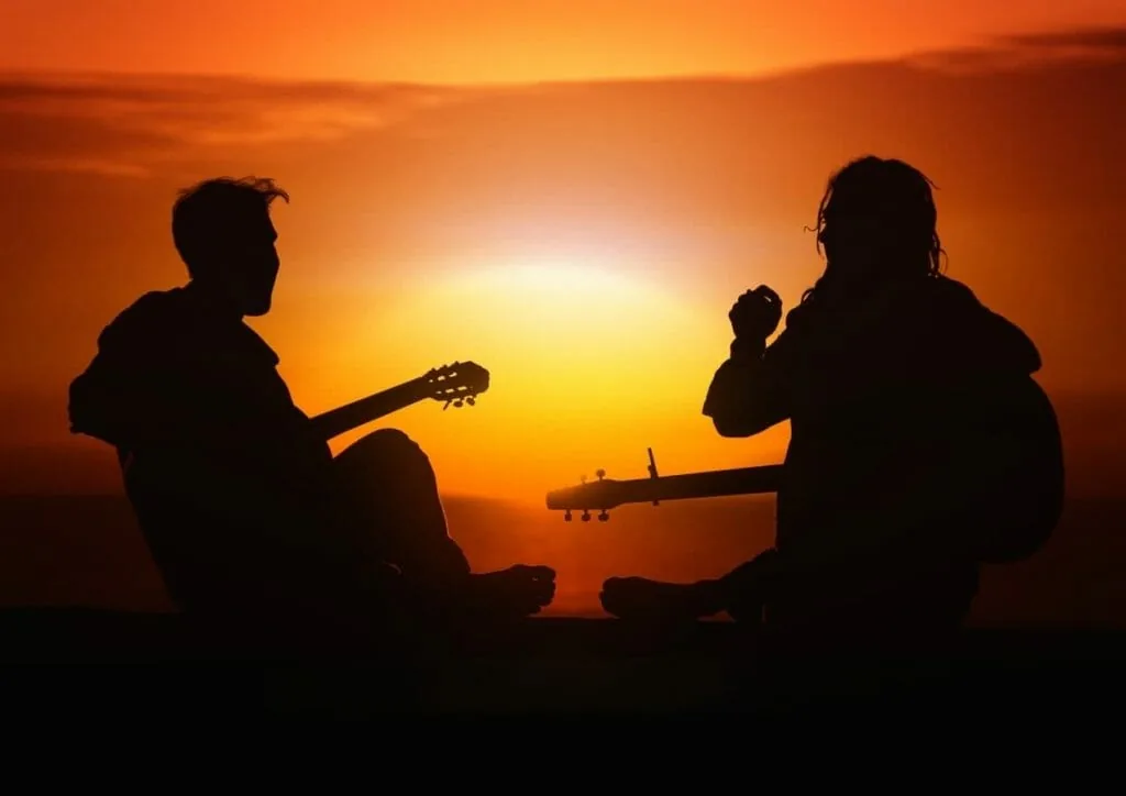 Letting one person see the real you: two friends sit facing each other with guitars, silhouetted against an orange sunset