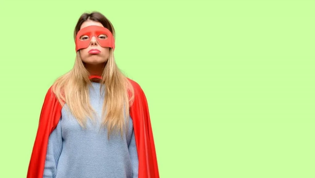 Tired of being strong: a young woman in a red superhero mask and cape looks worn out and fed up against a plain green background