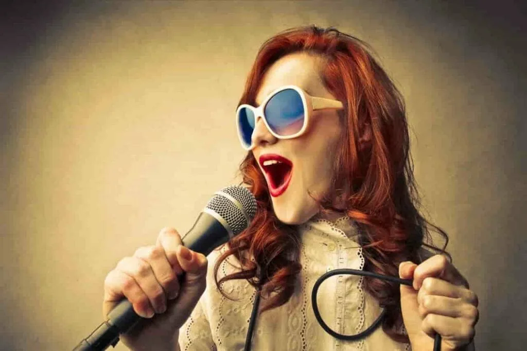 Living through stars: a red-haired woman in white sunglasses singing into a microphone