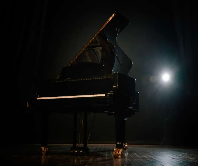Steps of the piano method: a black grand piano waiting on a dark wooden stage, lit by a single spotlight