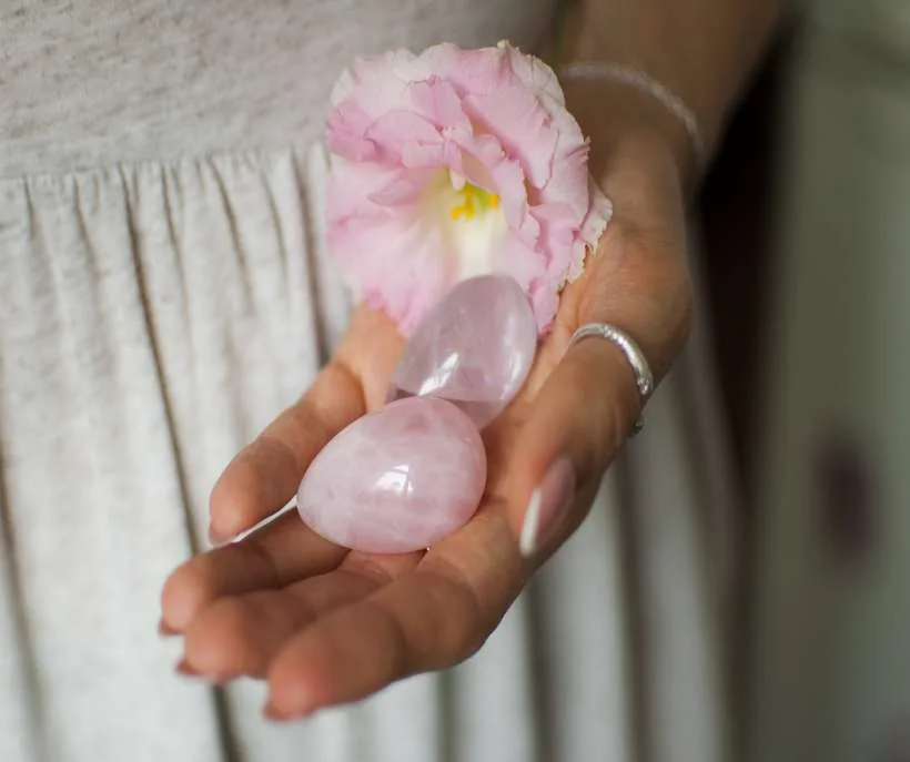 Rose quartz for shifting: a hand holding two smooth rose quartz eggs and a pink flower