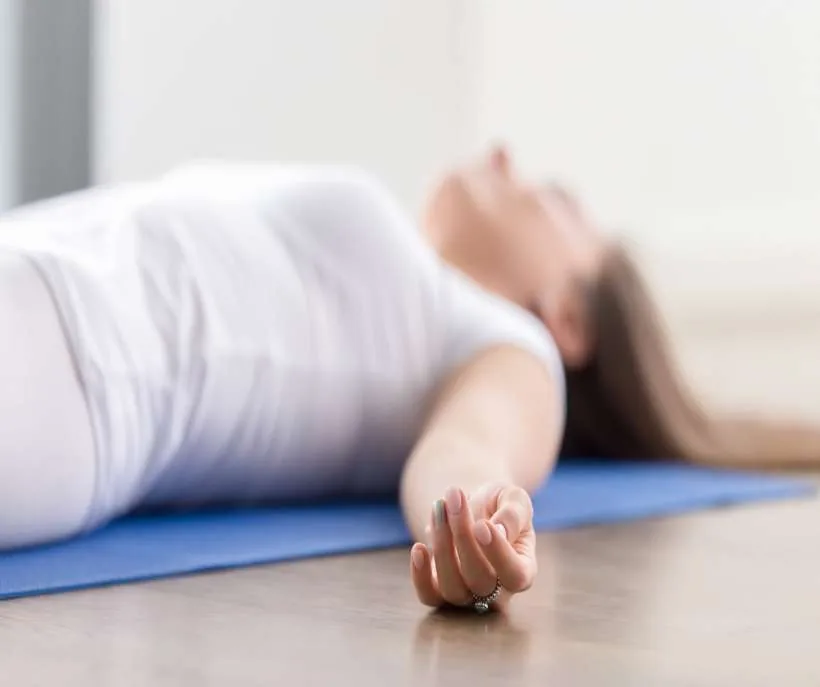 Starfish position for shifting: a woman resting on her back on a yoga mat with one arm loose beside her