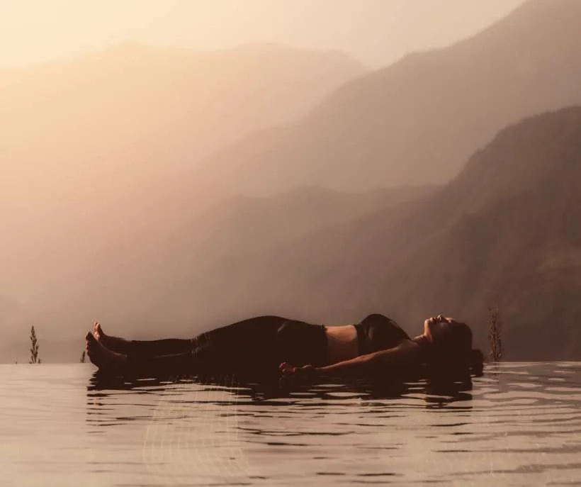 Starfish position waiting room idea: a woman floating on her back on calm water with misty mountains behind her