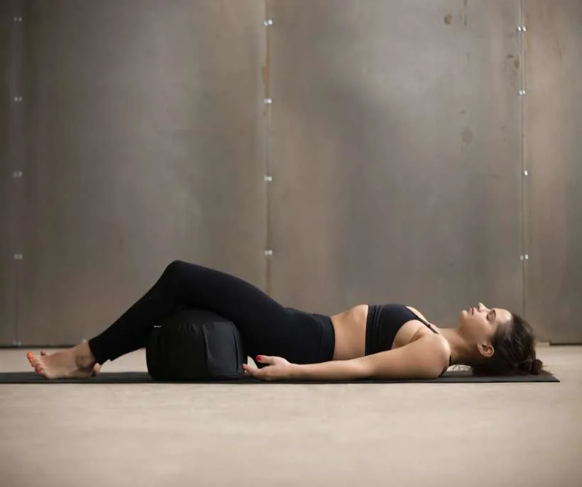 Supporting your neck and back in the starfish position: a woman lying on a mat with a bolster under her knees