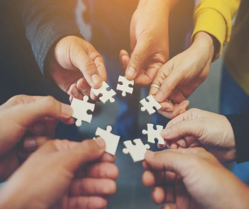 Hands of several people joining white jigsaw pieces in a circle, meeting future friends where they already are