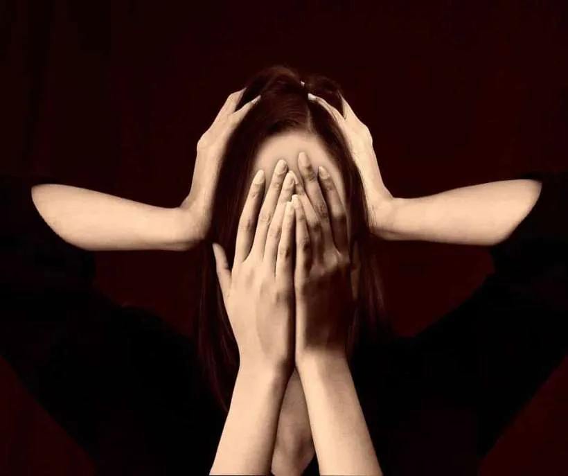 Mental and emotional ascension symptoms: a young woman covering her face with her hands as more hands grip her head