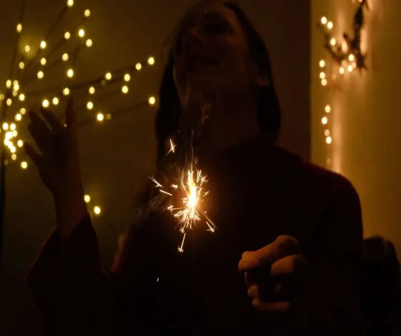 Universe prayers for gratitude: a young woman holding a lit sparkler among glowing fairy lights