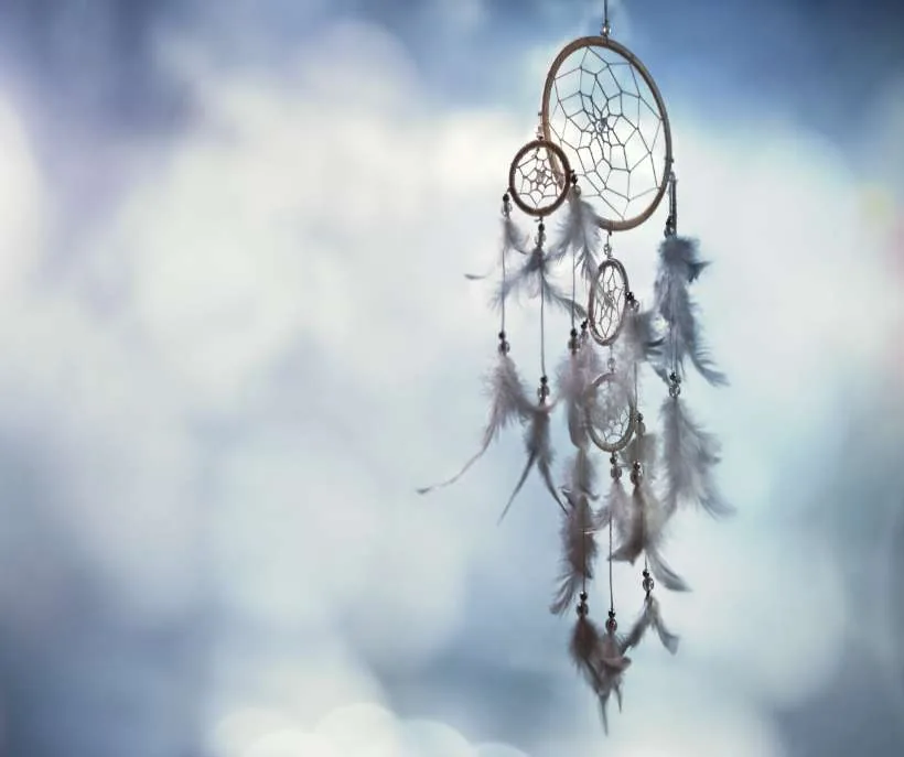 Universe prayers for protection: a feathered dreamcatcher hanging against a soft, cloudy blue sky