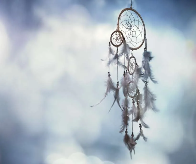 Spirit guides talking with you in sleep: a feathered dreamcatcher hanging against a soft, cloudy blue sky