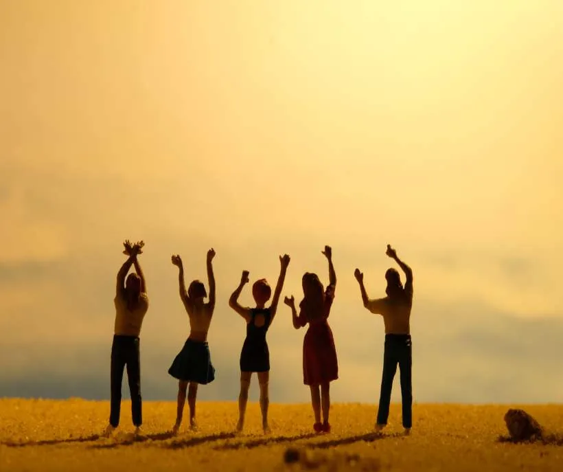 Five small figurines raising their arms on golden sand at sunset, like a happy group of friends you hope to manifest